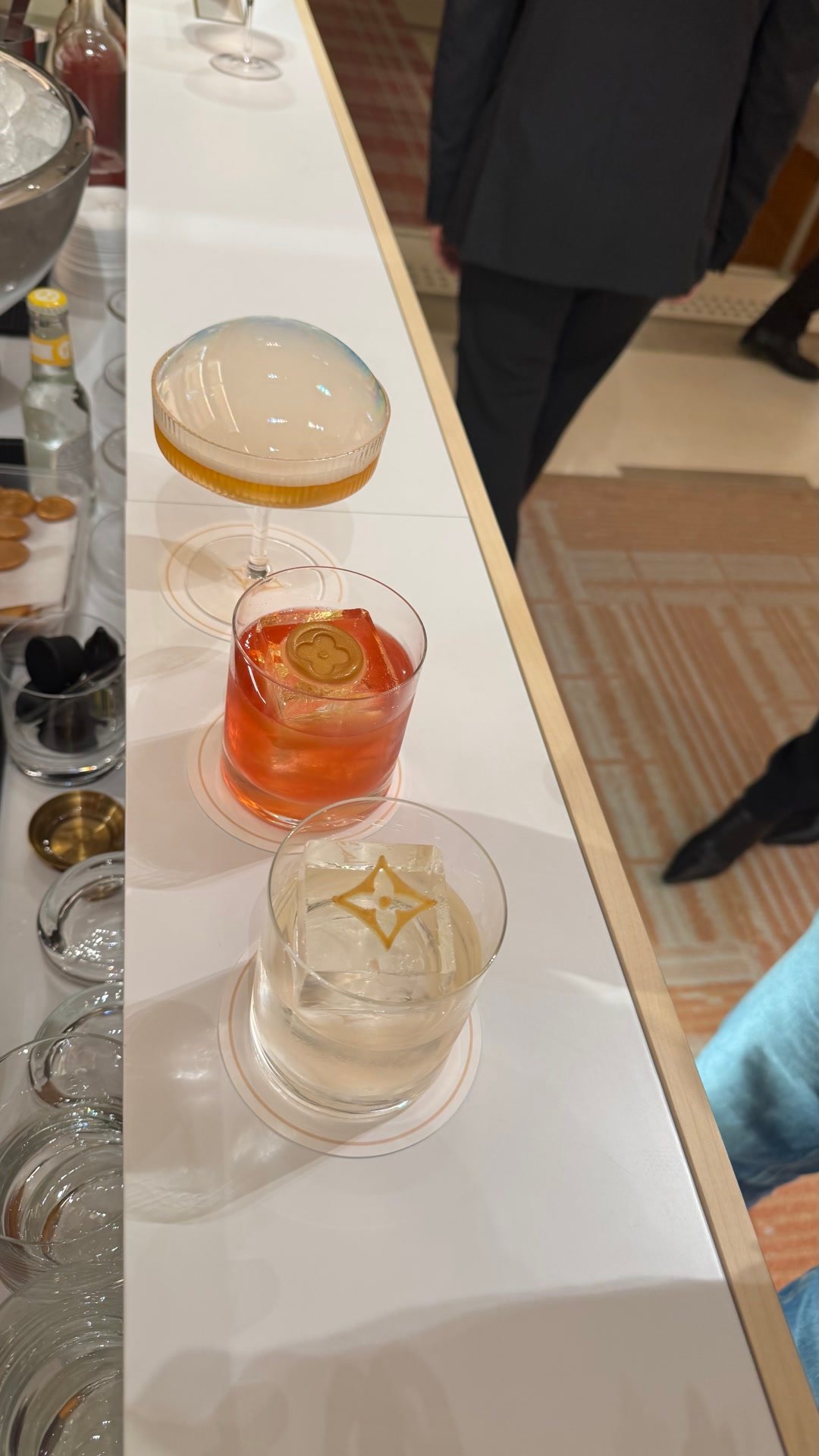 Deux cocktails posés sur un bar blanc, chacun avec un glaçon gravé d'un monogramme doré